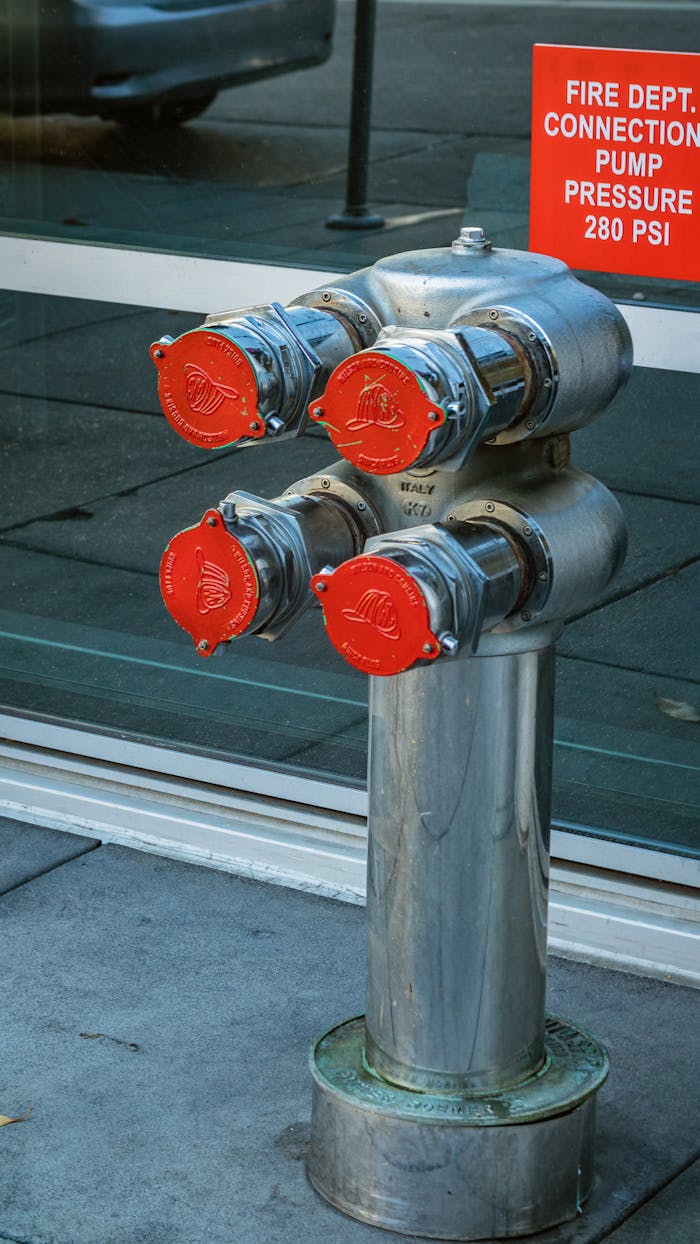 services-01 Vertical shot of an urban fire hydrant with red connection caps on a city sidewalk.